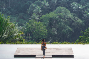 A beautiful girl practices yoga by the pool in the morning in Bali, Indonesia. Young woman in sportswear near the infinity pool against the backdrop of a tropical landscape.